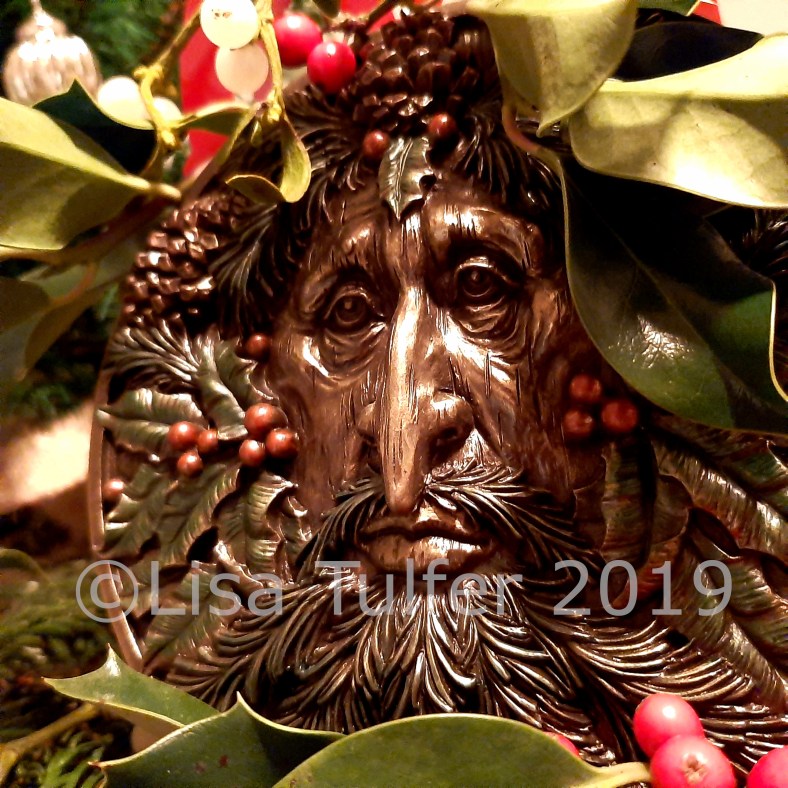 Colour photograph of Yuletide Green Man plaque surrounded by holly.  Image Copyright Lisa Tulfer 2019