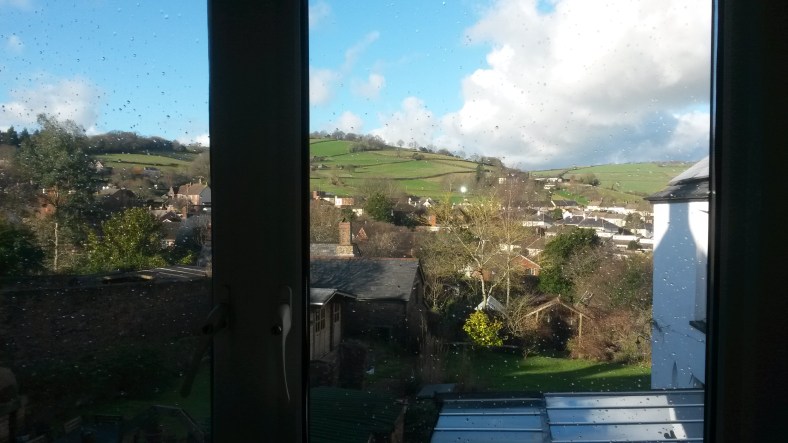 View from window, showing rooftops and distant grassy hills.